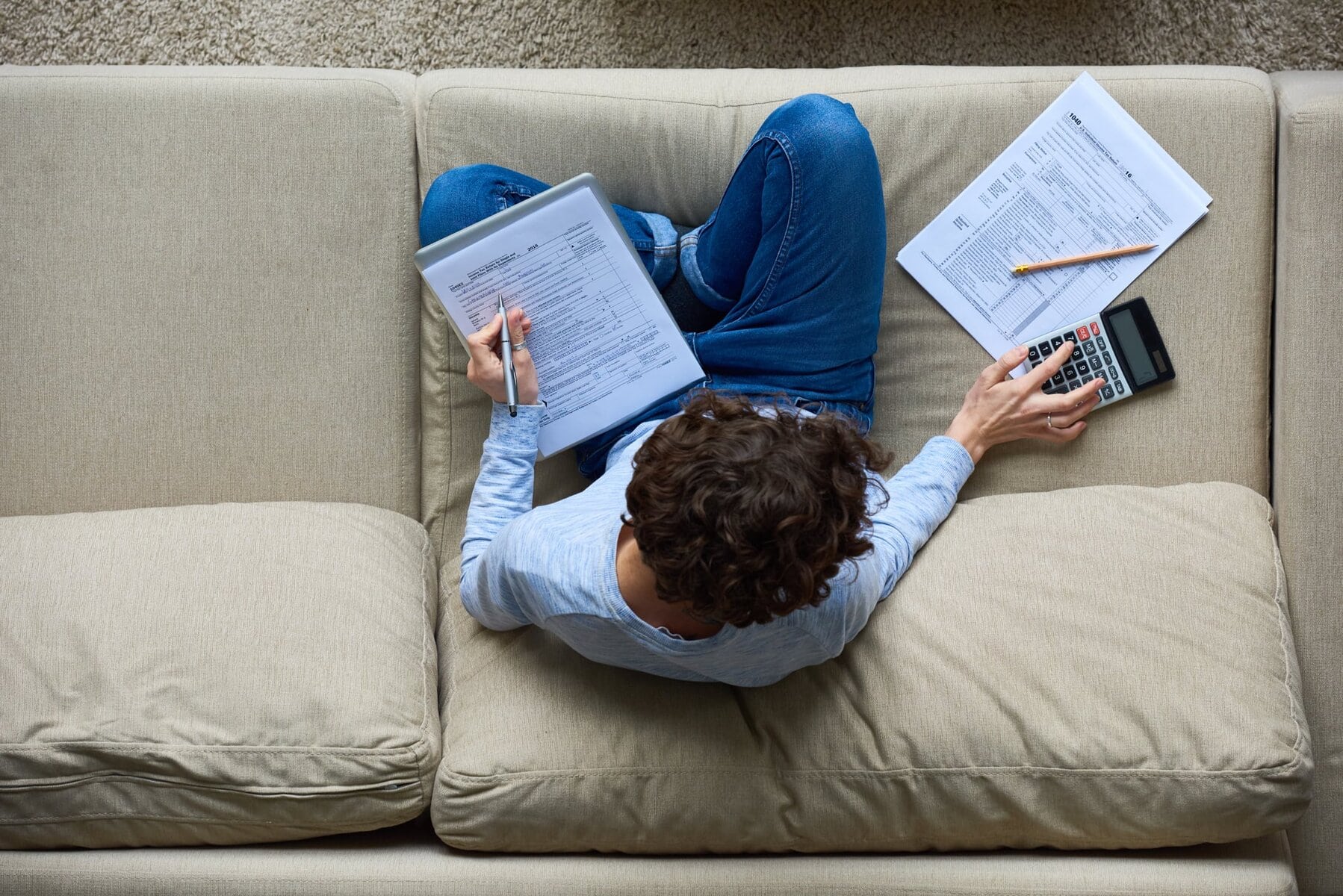 Person working on blockchain documents with calculator and pen on sofa.