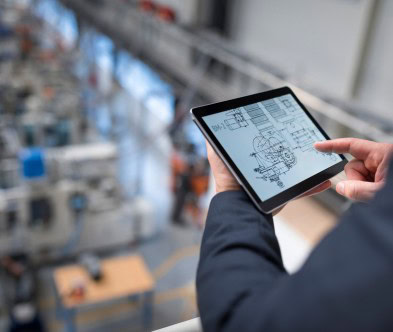 Person using a tablet with technical drawings in an industrial setting.