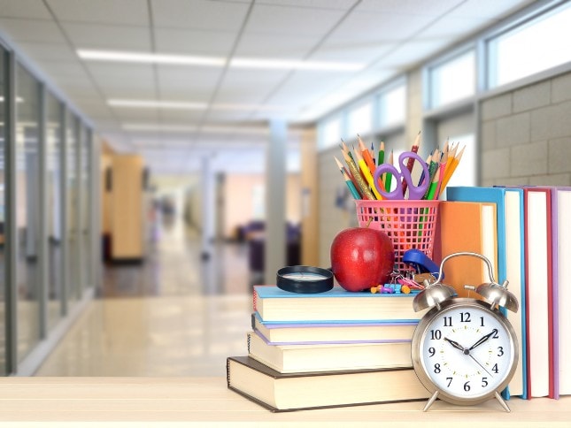 Educational supplies on a school desk with books, clock, and stationery.
