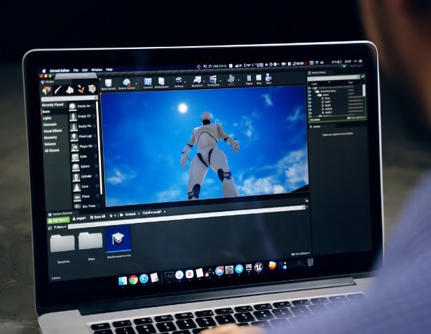 Laptop screen showing game development software with a robot character in a blue sky background.