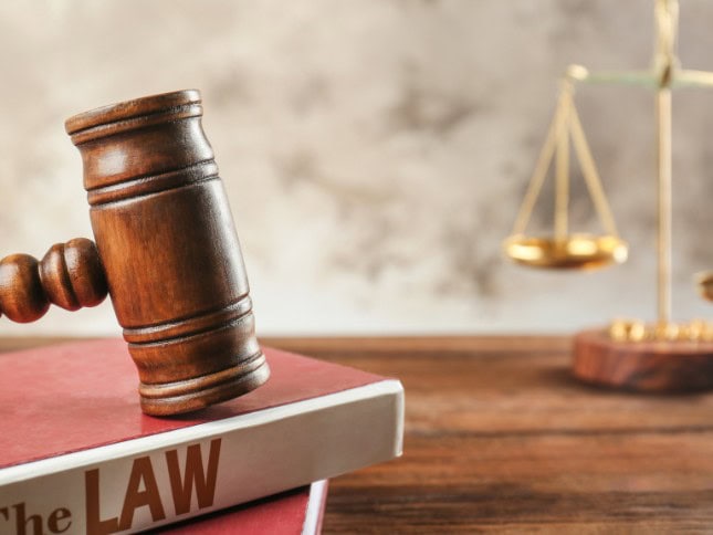 Wooden gavel resting on a law book with scales of justice in the background.