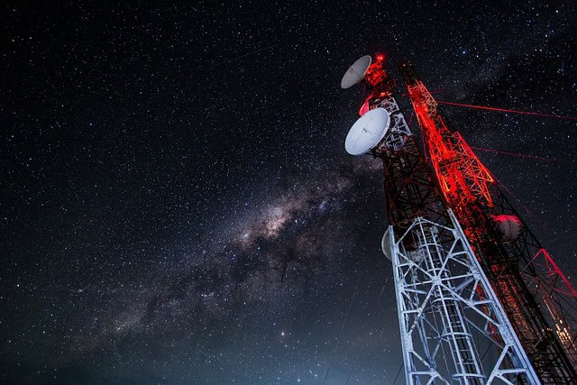 Telecommunication tower with satellite dishes under a starry sky.