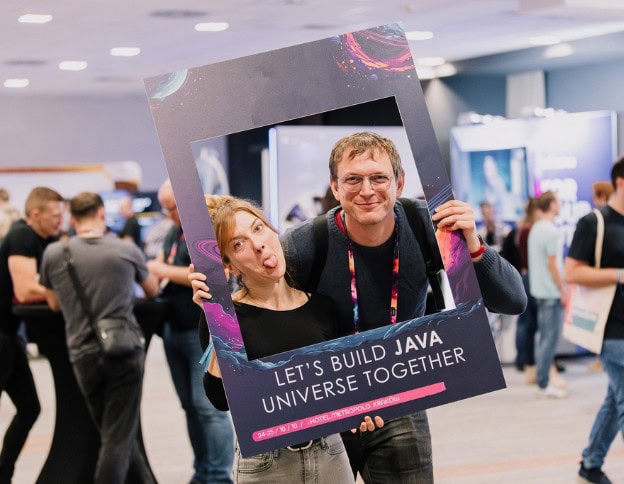 Two people holding a frame with "Let's Build Java Universe Together" at a tech event.