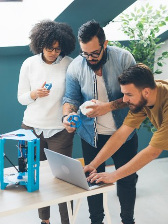 Team of developers working on AI and machine learning projects with a laptop and 3D printer.