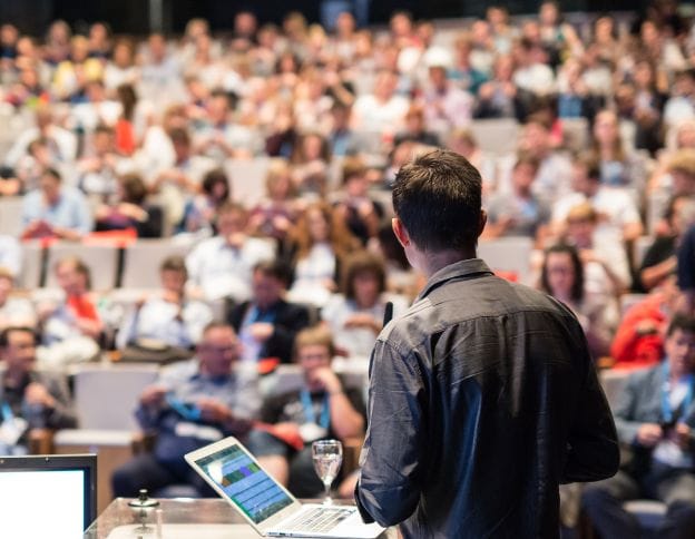 Speaker presenting on webhooks and event-driven architectures to a large audience.
