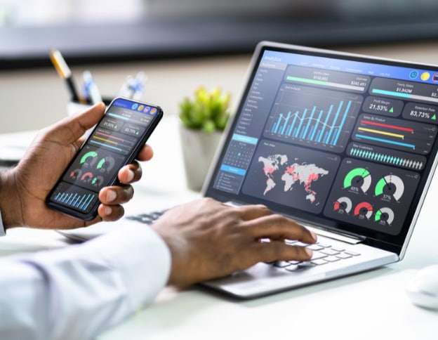 Person analyzing data on smartphone and laptop with dashboards and charts.