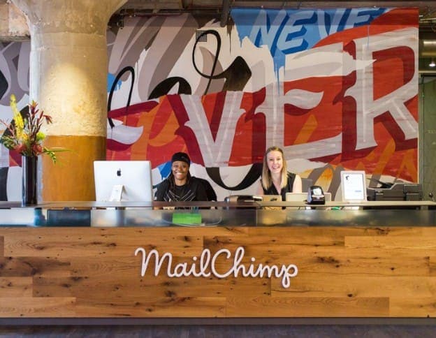 Modern office reception with two smiling staff members at MailChimp desk.