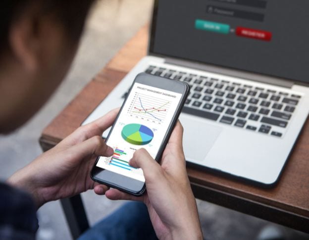Business analytics on smartphone with laptop showing operational data.