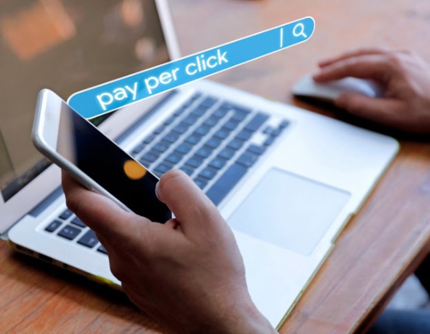 Person using smartphone for PPC advertising with laptop in background.