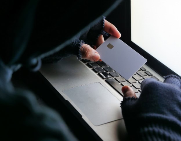 Person holding a credit card near a laptop, emphasizing cybersecurity.