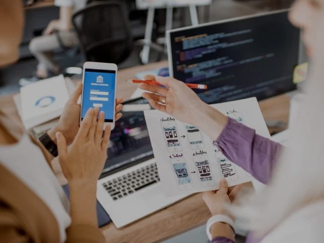 Team working on mobile app development with laptops and design sketches.