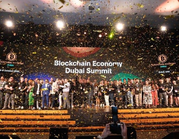 A large group of professionals and speakers gather on stage at the Dubai Blockchain Economy Summit.