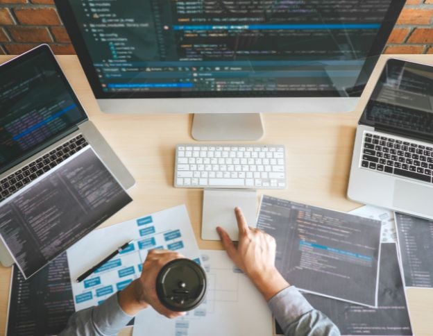 Software developer working with multiple screens and code on a desk.