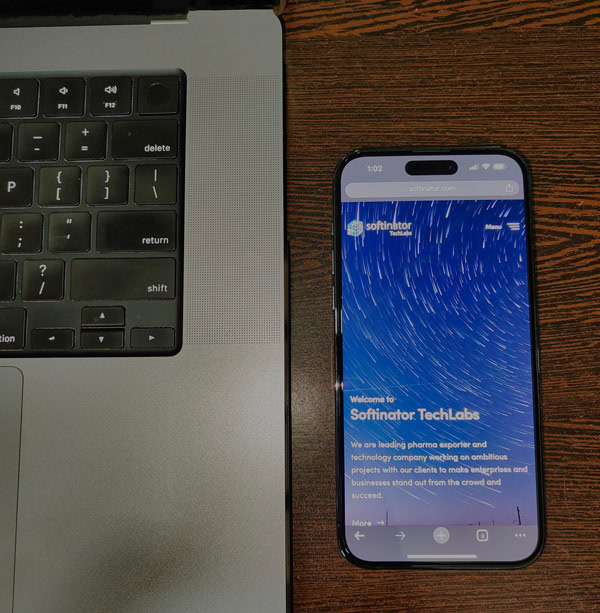 Smartphone displaying Softinator TechLabs app on wooden desk with laptop keyboard.