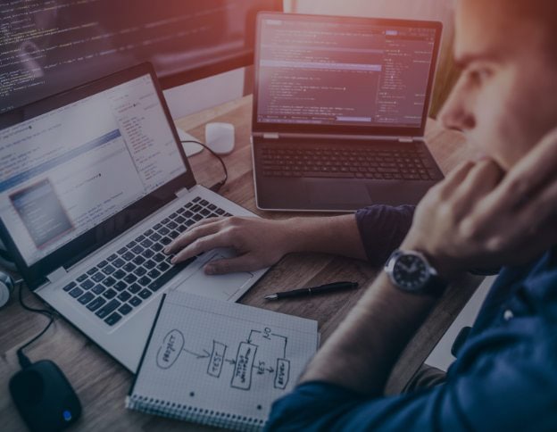 Software developer working on mobile app code on laptops and notes.