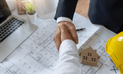 Business handshake between two professionals over architectural plans and blueprints.